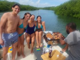 A lively group enjoys a barbecue on a boat, surrounded by lush mangroves — perfect for a fun day on the water with friends.