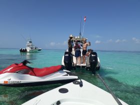 A lively group enjoys a day on the water, posing on a boat with a jet ski in the foreground — perfect for adventure seekers and water enthusiasts.