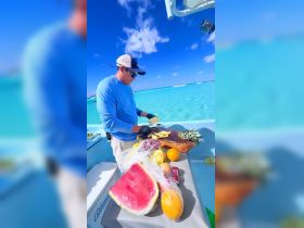 A crew member prepares fresh fruit on a boat, showcasing a vibrant selection of snacks perfect for a day on the water.