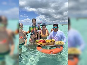 A joyful family enjoys a refreshing fruit platter while swimming in crystal-clear waters, capturing the essence of a fun-filled day on the water.