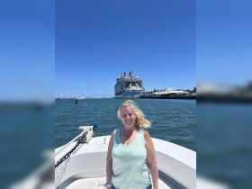 A woman smiles on a boat with a cruise ship in the background, capturing a joyful moment on the water.