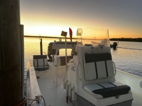 A serene view of the interior seating area of a boat at sunset, showcasing the helm and comfortable seating, perfect for a relaxing day on the water.
