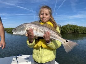A young girl proudly holds up her catch of the day while fishing, showcasing the excitement of a successful fishing trip.