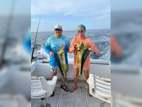 A successful fishing trip with two anglers proudly displaying their catch of mahi-mahi aboard a boat, showcasing the excitement of ocean fishing adventures.