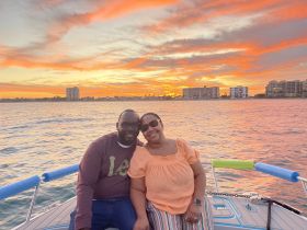 A couple enjoys a romantic moment on a boat at sunset, surrounded by vibrant colors and a serene waterfront view — perfect for memorable date nights or special celebrations.