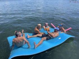 A lively group enjoys a fun day on the water, interacting with a starfish while lounging on a floating mat — perfect for summer adventures and snorkeling experiences.