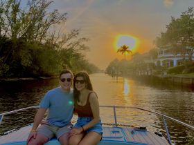 A couple enjoys a romantic sunset on a boat, surrounded by lush greenery and waterfront homes — a perfect moment for intimate getaways.