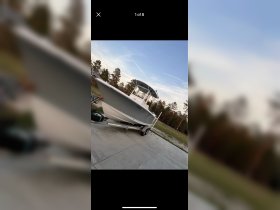 A sleek boat is showcased in a side view, parked on a trailer against a backdrop of trees, perfect for fishing or leisure outings.