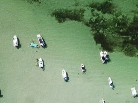 An aerial view of several boats anchored at a sandbar, with people enjoying the clear waters — a perfect scene for a fun day on the water.
