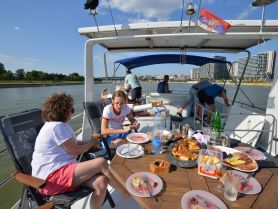 A lively group enjoys a meal aboard a boat, featuring a spread of delicious food and drinks, perfect for a fun day on the water.