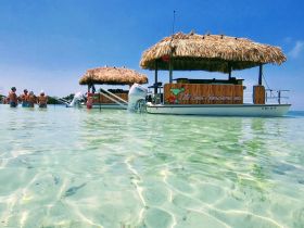 A lively group enjoys a sandbar stop around a tiki boat, creating the perfect atmosphere for fun in the sun and refreshing swims in crystal-clear waters.