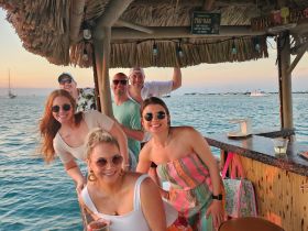 A lively group enjoys drinks at a tiki bar, capturing a fun moment against a beautiful sunset backdrop — perfect for celebrations and gatherings on the water.