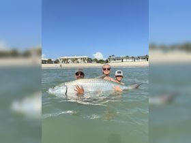 A family proudly displays a large tarpon caught during a fishing trip, showcasing a memorable wildlife encounter in the water.