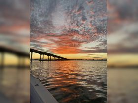 A stunning sunset casts vibrant colors over the water, with a bridge silhouetted against the sky — a perfect backdrop for evening boat trips.