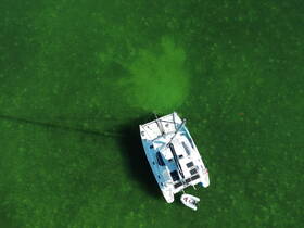 Aerial view of a sleek catamaran cruising over vibrant green waters, showcasing the beauty of boating in nature.