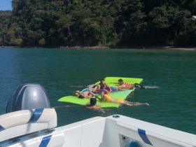A lively group enjoys a sunny day on a floating mat in the water, perfect for family fun and relaxation during a boating trip.