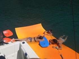 A lively group enjoys a sunny day on a floating mat, relaxing and having fun in the water — perfect for summer outings and water adventures.