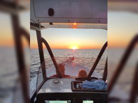 A serene sunset view from the helm of a boat, showcasing a couple enjoying the tranquil waters — perfect for romantic evening cruises.