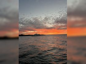A stunning sunset view featuring a yacht silhouetted against vibrant orange and pink skies, creating a picturesque scene perfect for evening cruises.