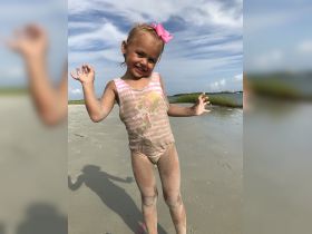 A joyful child plays on the beach, covered in sand and smiling brightly — a perfect moment capturing the fun of a day by the water.