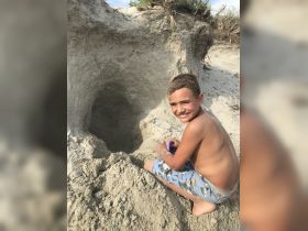 A child enjoys building a sand structure on the beach, capturing the essence of fun and creativity in a sunny outdoor setting.