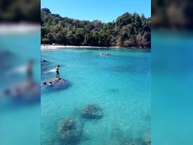 A vibrant scene at a beautiful beach with people swimming and kayaking in crystal-clear waters, showcasing the perfect day for outdoor adventures.