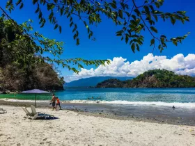 A picturesque beach scene with families enjoying the sun and surf, showcasing the stunning coastline and clear waters — perfect for a family day out.