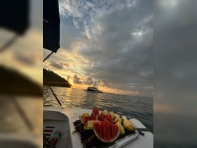 A vibrant display of fresh watermelon and pineapple on a boat, set against a stunning sunset backdrop — perfect for enjoying tropical snacks while cruising.