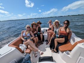 A lively group of friends enjoys a sunny day on the water, relaxing on a boat with drinks in hand — perfect for a fun day out with friends.