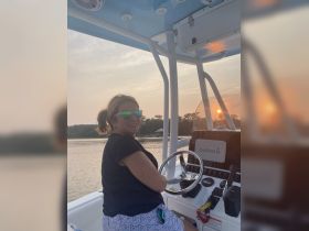 A woman enjoys steering a boat at sunset, capturing the essence of a perfect evening on the water.
