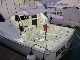 A crew member cleans the interior of the 'Big Tuna' boat, showcasing the well-equipped helm and seating area, perfect for fishing trips or leisure outings.