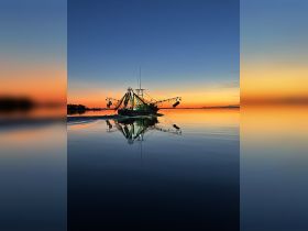 A serene sunset view of a fishing boat reflecting on calm waters, showcasing the tranquil beauty of maritime life.