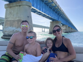 A joyful family enjoys a day on the water, posing together under a scenic bridge — perfect for memorable boating adventures.
