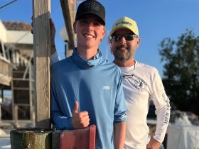 A young man and an adult pose together, smiling at the camera, capturing a joyful moment before a fishing adventure.
