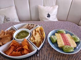 A beautifully arranged platter of snacks featuring chips, guacamole, and a colorful fruit display, perfect for enjoying on a boat trip.