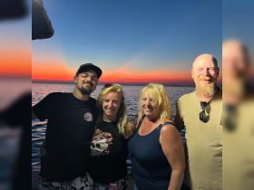 A cheerful group poses together against a stunning sunset backdrop on the water, capturing a memorable moment during their boating adventure.