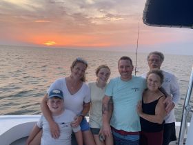 A joyful family poses together on a boat at sunset, capturing a memorable moment during their ocean adventure.