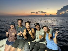 A cheerful group of friends poses on a boat at sunset, capturing a moment of joy and camaraderie on the water.