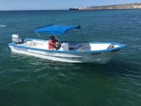 A man navigates the Cleo boat through clear waters, showcasing a perfect day for fishing or exploring the coastline.