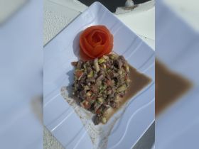 A beautifully plated dish featuring a fresh ceviche with a decorative tomato rose, perfect for onboard catering during a luxurious boat trip.