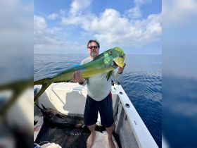 A proud angler holds up a vibrant mahi mahi catch aboard a fishing boat, showcasing the thrill of deep-sea fishing in open waters.