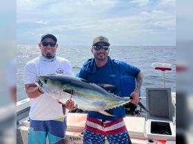 Two anglers proudly display their catch of the day, a large tuna, while enjoying a successful fishing trip on the open water.