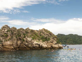 A lively group enjoys snorkeling near a rocky coastline, showcasing the beauty of marine life and adventure on the water.