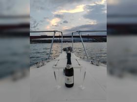 A bottle of champagne and two glasses are elegantly displayed on the deck of a boat, set against a scenic backdrop of a bridge and cloudy sky — perfect for a romantic evening on the water.