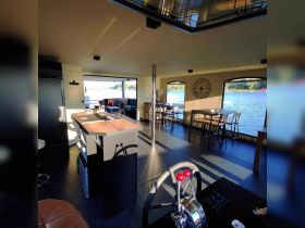 Interior view of a stylish boat cabin featuring a bar area, seating, and a helm, offering a comfortable space for relaxation and socializing while enjoying the waterfront scenery.