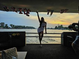 A bride-to-be poses with a drink against a stunning sunset backdrop, celebrating with friends on a boat — perfect for bachelorette parties and memorable moments on the water.