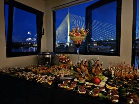 An elegant display of gourmet appetizers and cocktails set against a stunning nighttime view of a bridge, perfect for upscale dining experiences on a boat.