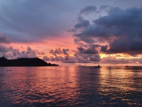 A breathtaking sunset paints the sky in vibrant hues over a tranquil coastline, creating a picturesque backdrop for evening boat adventures.