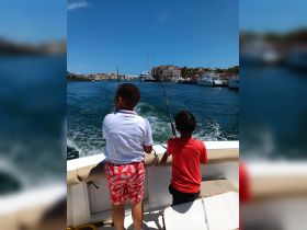 Two children enjoy a fishing trip on a boat, casting their lines while surrounded by a scenic marina — a perfect family adventure on the water.