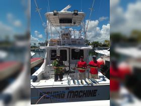 A group of anglers proudly displays their catch aboard the 'Fishing Machine' in Santo Domingo, showcasing a successful fishing trip under the sunny skies.